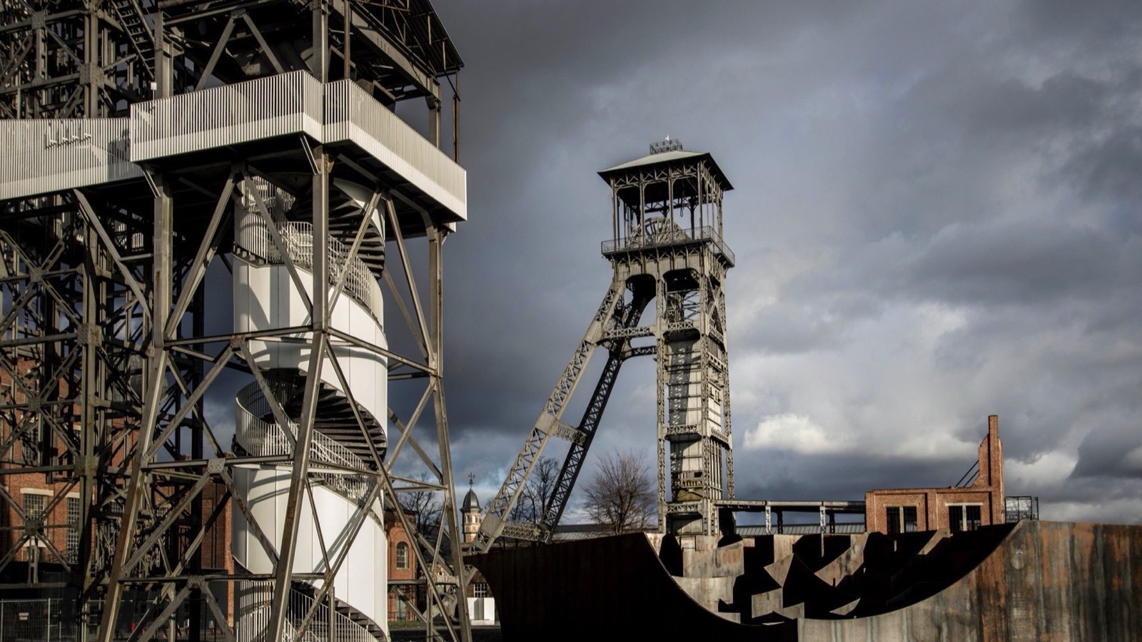 The steel winding towers of the former Winterslag colliery at C-mine, Genk, under a dark sky.