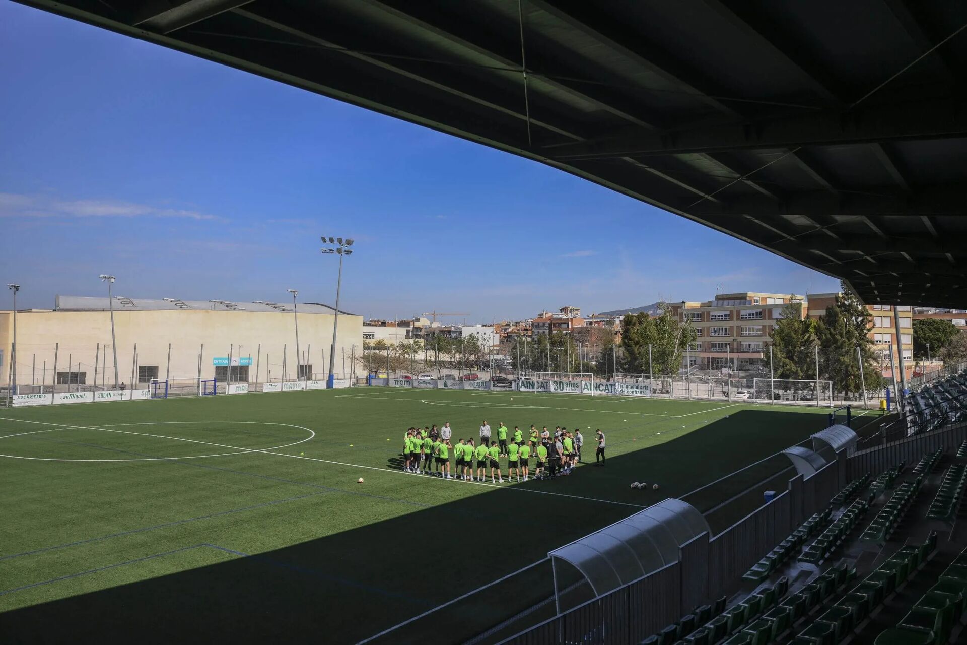 Football players gathered on a training pitch, viewed from a covered stand
